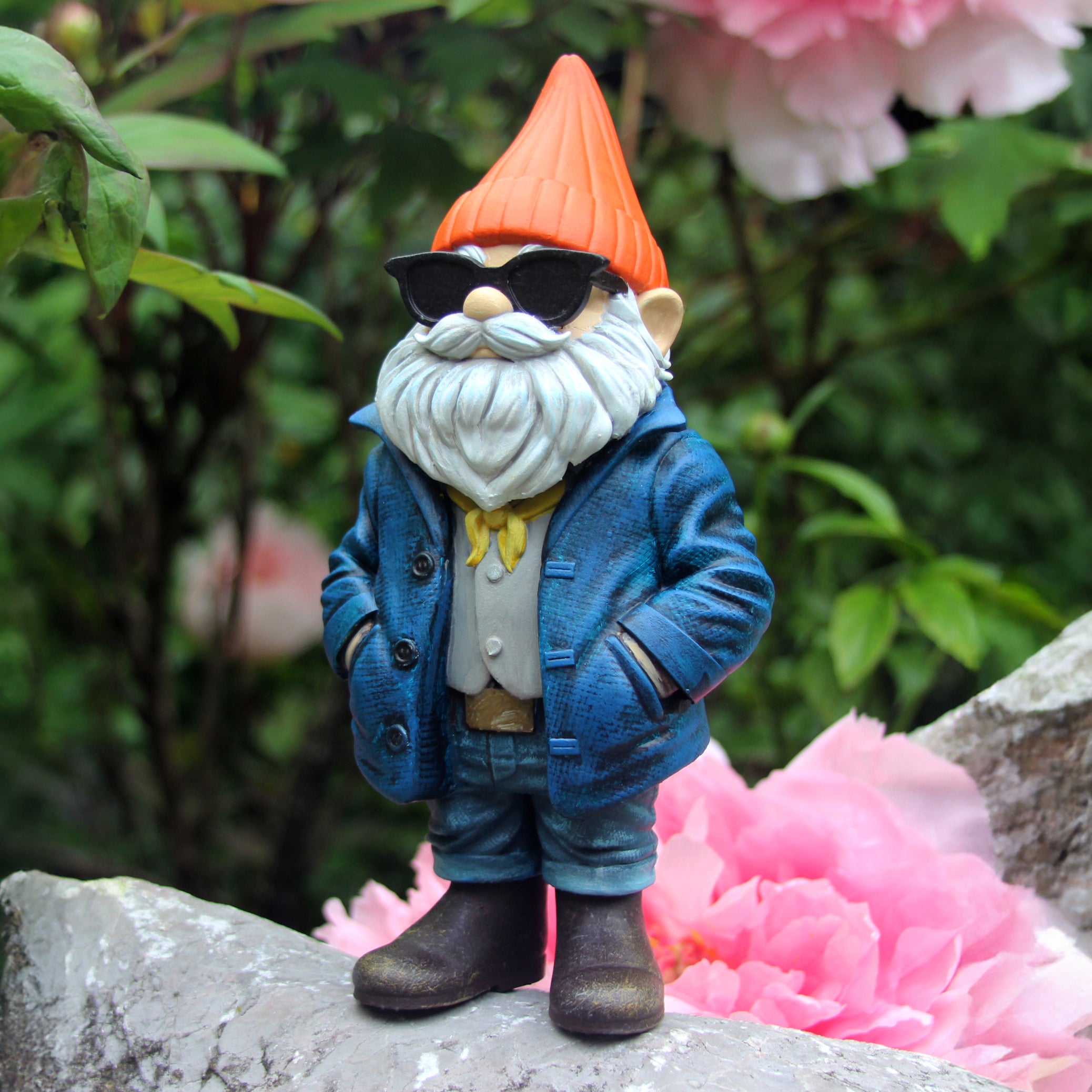 Garden gnome with sunglasses and a blue coat standing on a rock with pink flowers in the background